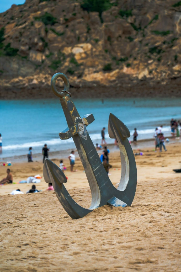 Large anchor on a sandy beach with ocean background